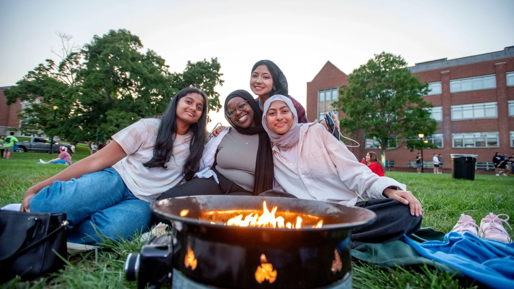 Four female students gathered around fire pit posing for photo.